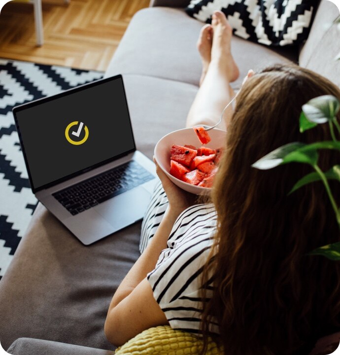 Žena jí na pohovce meloun a používá notebook se spuštěnou aplikací Norton 360 AntiVirus Plus.